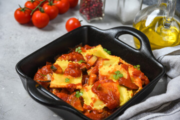 Ravioli tomato sauce on black pan on a wooden board. food delivery from restaurant to home.  top view, pasta recipe  Italian cuisine.