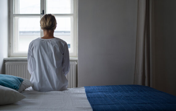 Rear view of woman patient sitting on bed in hospital feeling stressed, mental health and coronavirus concept.