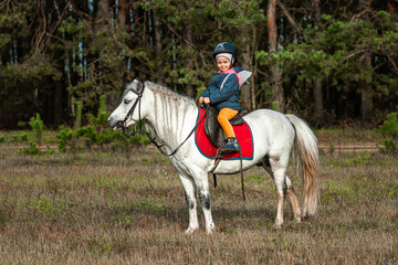 Little girl on a white pony on a background of nature. Jockey, hippodrome, horseback riding.