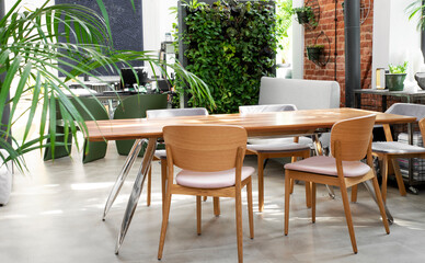 Stylish table and chairs in loft apartment in industral style with wall from bricks and vertical garden. Interior of dining room in apartment at home.