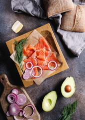 Ingredients for making healthy sandwich. Rye bread bun, salmon, avocado, onion, dill and lemon. Top view.