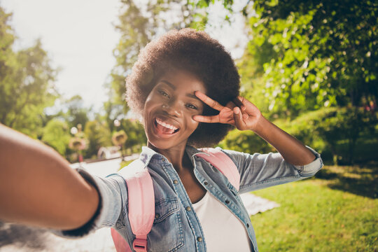 Photo portrait of black skinned beautiful girl taking selfie in summer park smiling showing v-sign peace wearing casual jeans clothes