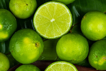 Close up pile of half and whole fresh lime juicy on green banana leaves with clearly water drop on...