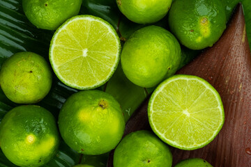 Obraz na płótnie Canvas Pile of half and whole fresh lime juicy on green banana leaves with clearly water drop on surface