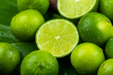 Close up pile of half and whole fresh lime juicy on green banana leaves with clearly water drop on...