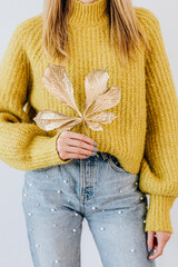 Woman in a yellow knitted sweater holding a golden crisp leaf