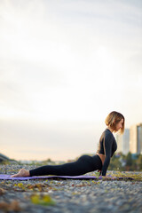 Fototapeta na wymiar good-looking young woman practicing asana on a yoga mat in city, alone, wearing black sportswear