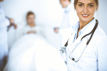 Female doctor smiling on the background with patient in the bed and two doctors