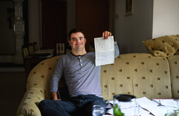 Down syndrome adult man sitting indoors at home, writing.