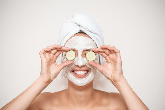 Funny smiling Spa Woman with towel wrapped around her head, applying fresh Facial Mask with cucumbers. Beauty Treatments. Face mask, skin care concept