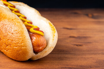 American traditional fast food Hotdog with fresh organic bread bun white wheat and black charcoal sausage ketchup mustard for meal with roasted onion pickle and French fries wedges and coleslaw