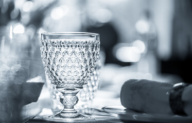 the table is set, black and white picture of a table setting with focus on the wine glass and a blurred background, surrounded by cutlery, plate and napkin, light is reflection from the empty glass 