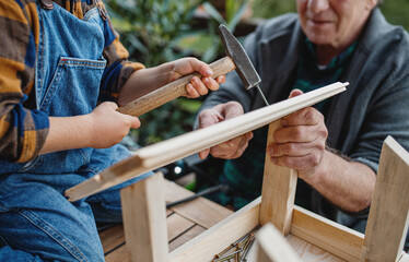 Unrecognizable small boy with senior grandfather constructing birdhouse, diy project.