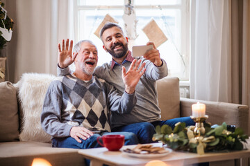 Mature man and senior father with smartphone indoors at home at Christmas, video call concept.