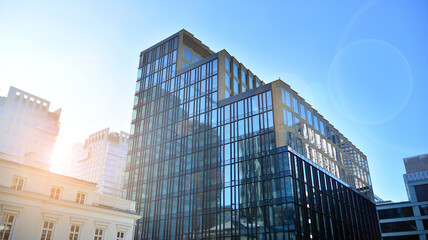 Blue curtain wall made of toned glass and steel constructions under blue sky. A fragment of a building. Glass facades on a bright sunny day with sunbeams in the blue sky.