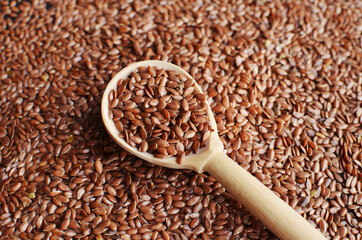 Uncooked raw flax seeds in wooden spoon on seeds background.