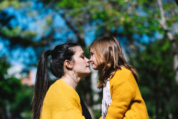 Fototapeta premium Little cute child baby girl kiss on cheek and hug, embrace with happy pretty woman in green park. Mother, little kid daughter. Mother's Day, love family, parenthood, childhood