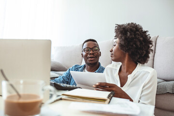 Young married couple doing their paperwork together, paying bills online. Focus on the guy. Loving young couple using laptop and analyzing their finances. Writing notes.