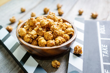 Flat lay of tasty caramel popcorn and clapperboard on wooden table, close up. Movie time concept