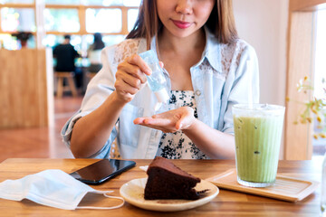 Young Asian woman applying hand sanitizer onto her hand before eating in cafe for disinfection...