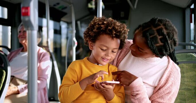 African-american boy playing with phone on mother lap inside bus