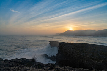 Fototapeta na wymiar huge storm surge ocean waves crashing onto shore and cliffs at sunrise with a person standing there