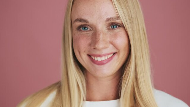 A surprised blonde woman is doing silence gesture standing isolated over pink background in studio