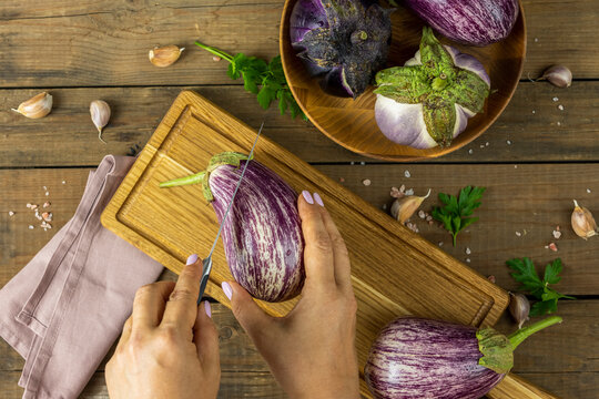 Woman hands cut the eggplant on wooden board. Dark wooden background. Concept of green house life style and products of subsistence farming, flat lay, copy space