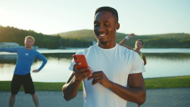 Happy African American Social Influencer Fitness Trainer Using Mobile Phone User Interface Cloud Technology while Active Couple Performing Cardio Exercises in Background. Smartphone Animation.