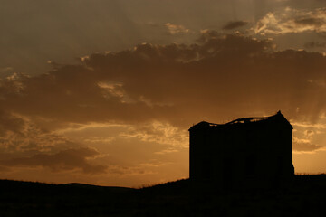 Casa en ruinas en el campo a contraluz durante el atardecer, con nubes en el cielo.