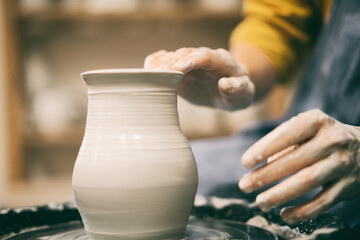 Woman makes pottery making in the workshop on a potter's wheel, hands in clay close-up