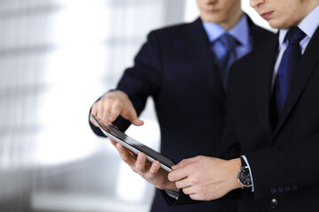 Business people use a tablet computer for discussion of their new project, standing in a modern office. Unknown businessman or male entrepreneur with a colleague at workplace. Teamwork and partnership