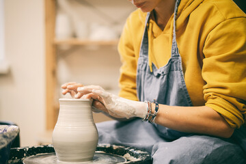 Woman makes pottery making in the workshop on a potter's wheel, hands in clay close-up