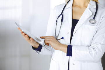 Unknown woman-doctor is holding a tablet computer in her hands, while standing in a clinic cabinet. Female physician at work, close-up. Perfect medical service in a hospital. Medicine concept