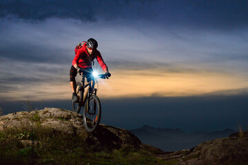 Naklejka na ściany i meble Cyclist Riding the Mountain Bike on Rocky Trail at Night. Extreme Sport and Enduro Biking Concept.