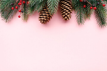 Green foam Christmas tree branch border with cones and red berries on the pink background