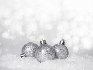 Three silver Christmas balls in the snow on an abstract bokeh background.