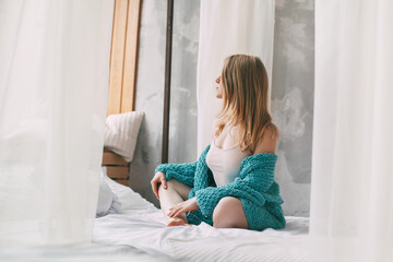 Cute girl sitting cross-legged on the bed in the morning. Young woman in pajamas sitting on the bed after waking up