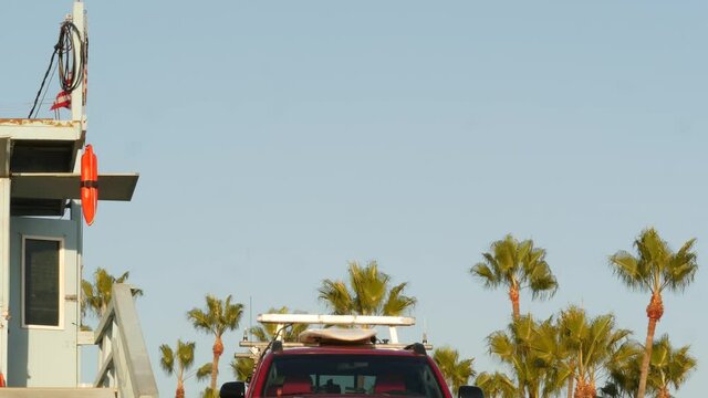 Iconic Retro Wooden Lifeguard Watch Tower, Baywatch Red Car. Life Buoy, American State Flag And Palm Trees Against Blue Sky. Summertime California Aesthetic, Santa Monica Beach, Los Angeles, CA USA.