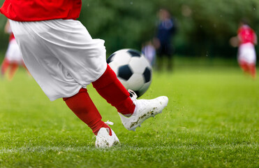 Football kick. Young player kicking soccer ball on green grass turf field. Closeup of footballers...