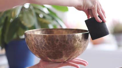 Woman playing on Tibetan singing bowl while sitting on yoga mat. Vintage tonned.