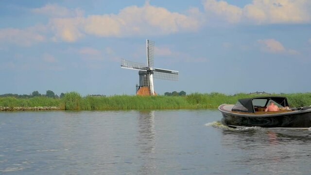 Dutch Old Windmill on a dike near the water, a small Dolly shot in slowmotion an other boat is sailing by from right to left.