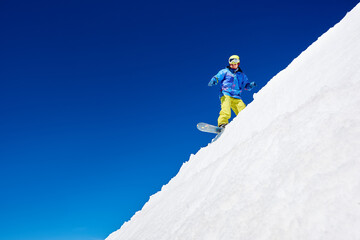 Active man snowboarder riding on white slope inhigh mountains at sunny day against blue sky. Ski...