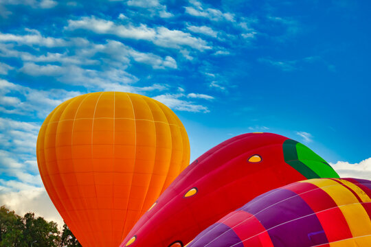 three balloons of orange red and multicolored colors against the blue sky with clouds