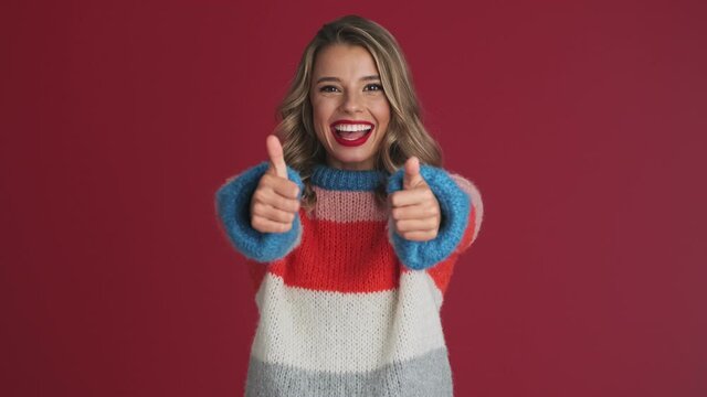 Young smiling woman showing thumbs up  gesture isolated over red wall background