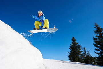 Jumping snowboarder keeps one hand on the snowboard on blue sky background. Ski season and winter sports concept