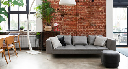Industrial living room with sofa in loft apartment with window and brick wall. Spacious interior of...