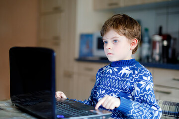 Fototapeta na wymiar Lonely kid boy learning at home on laptop for school. Adorable child making homework and using notebook and modern gadgets. Home schooling concept during pandemic corona virus lockdown quarantine