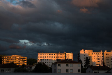 bâtiments d'une ville sous un ciel nuageux et sombre, illuminés et colorés en orange par un...