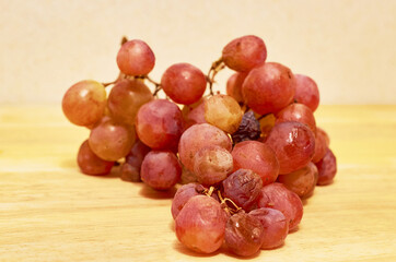A spoiled bunch of grapes lies on a wooden surface.
